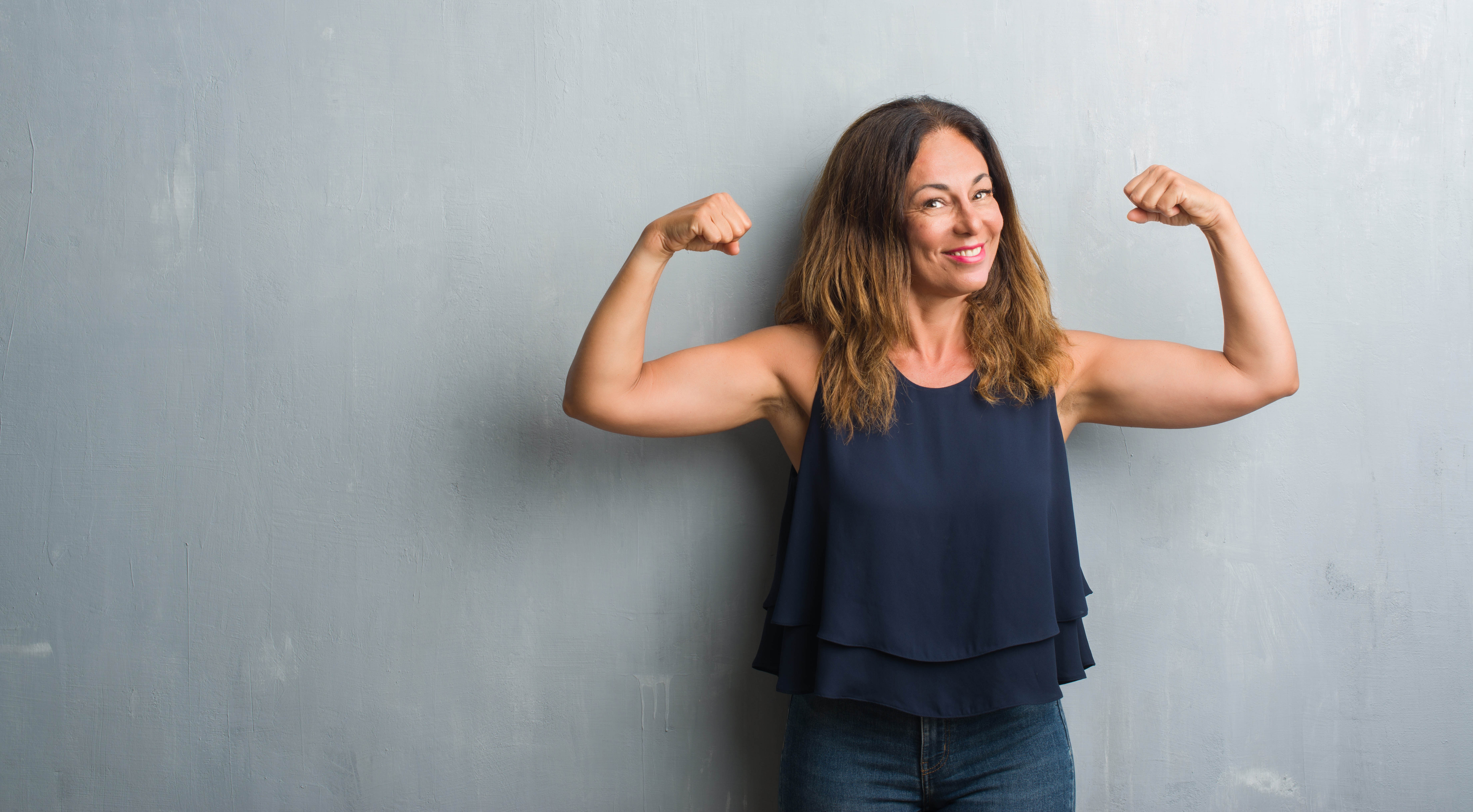 Strong, fit middle aged woman flexing in front of a grey background